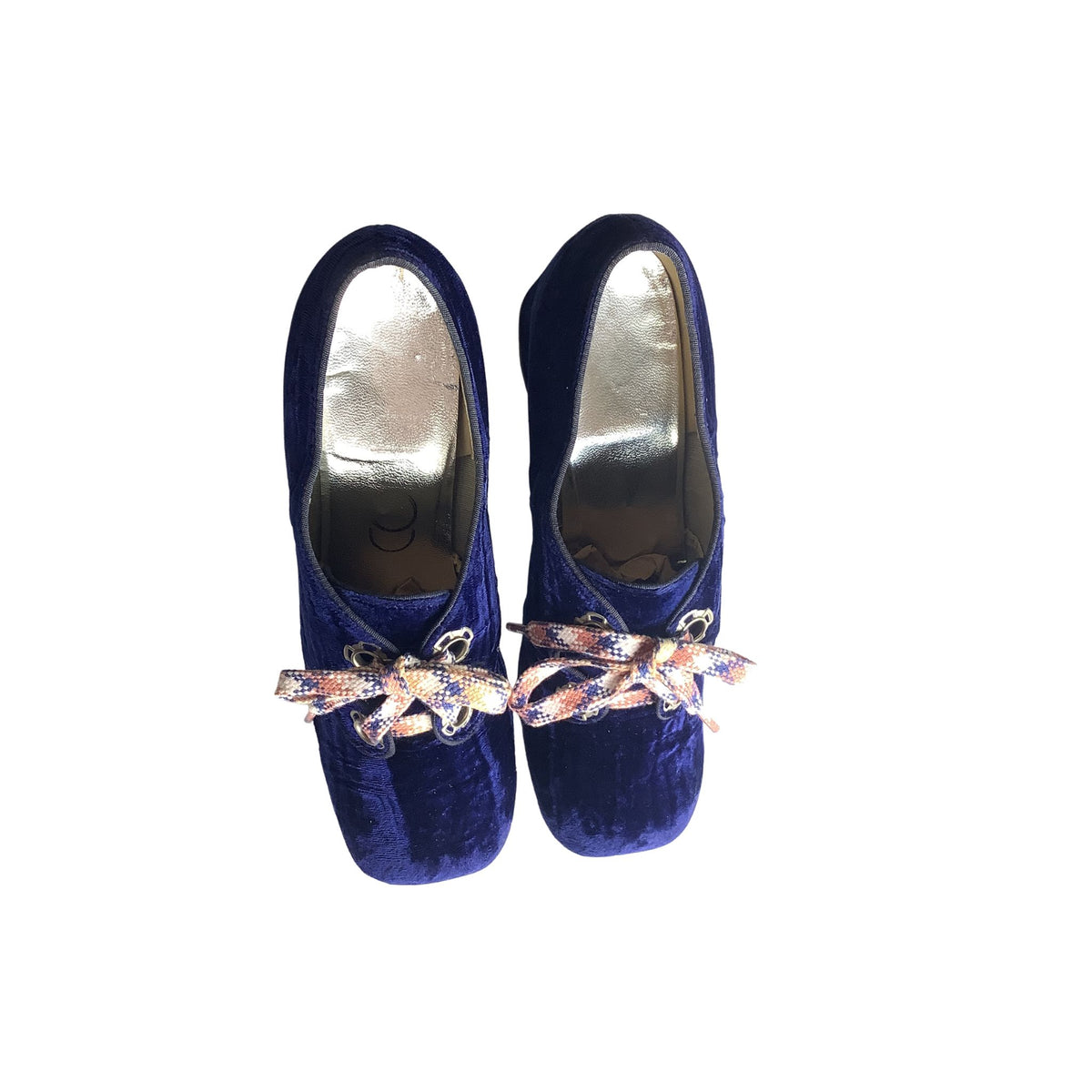 Interior view of a pair of blue velvet shoes with decorative bows on a white background