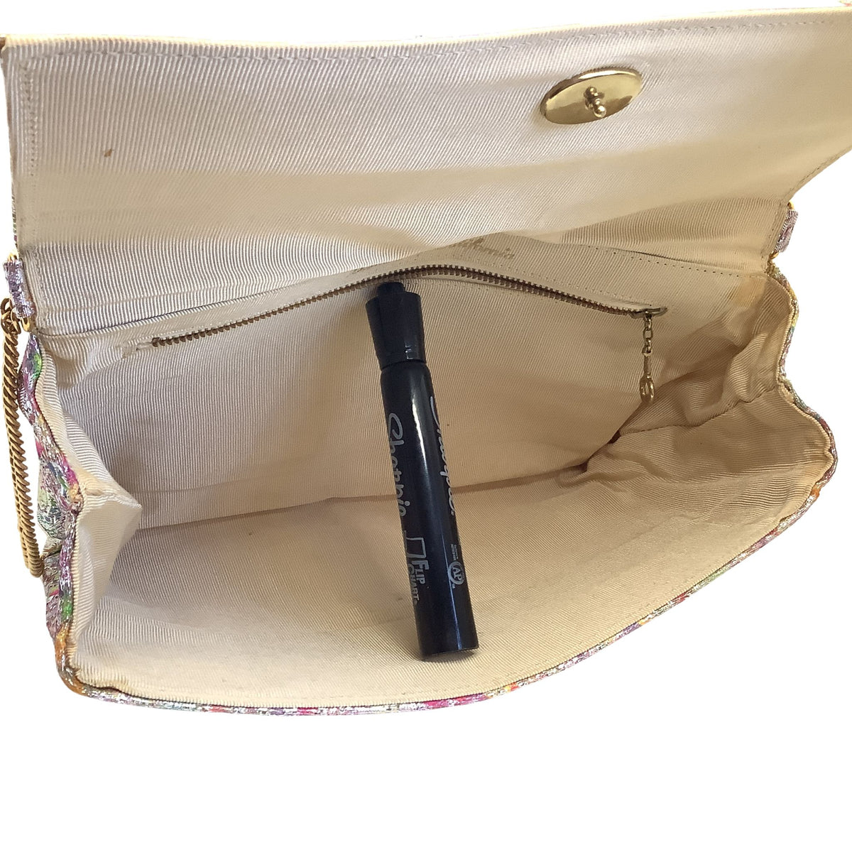 An open beige fabric handbag with a gold-tone snap closure and a small floral patterned edge, shown against a white background with a black pen placed inside to hold open.