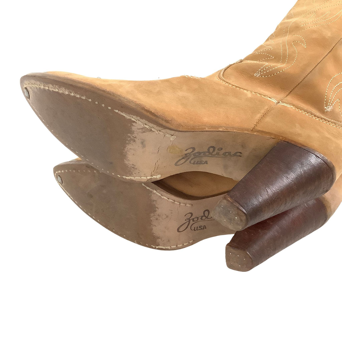 A tan suede cowboy boot shown from the back, revealing a worn brown sole and dark brown heel.