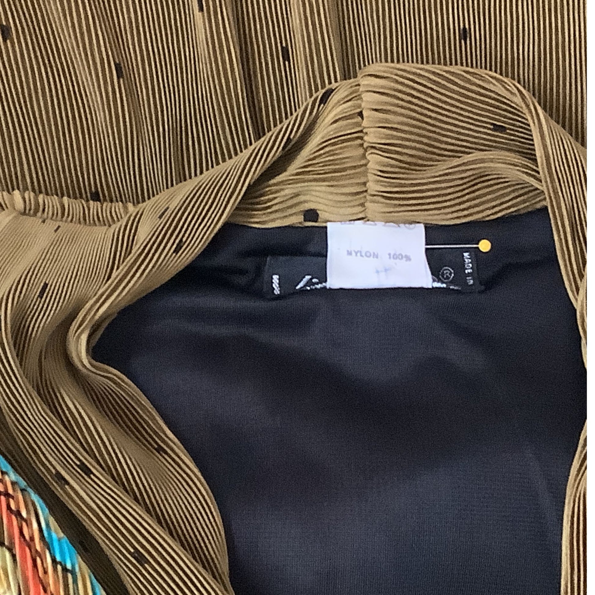 Close-up of a content label. Olive green mircro-pleat garment laid flat.