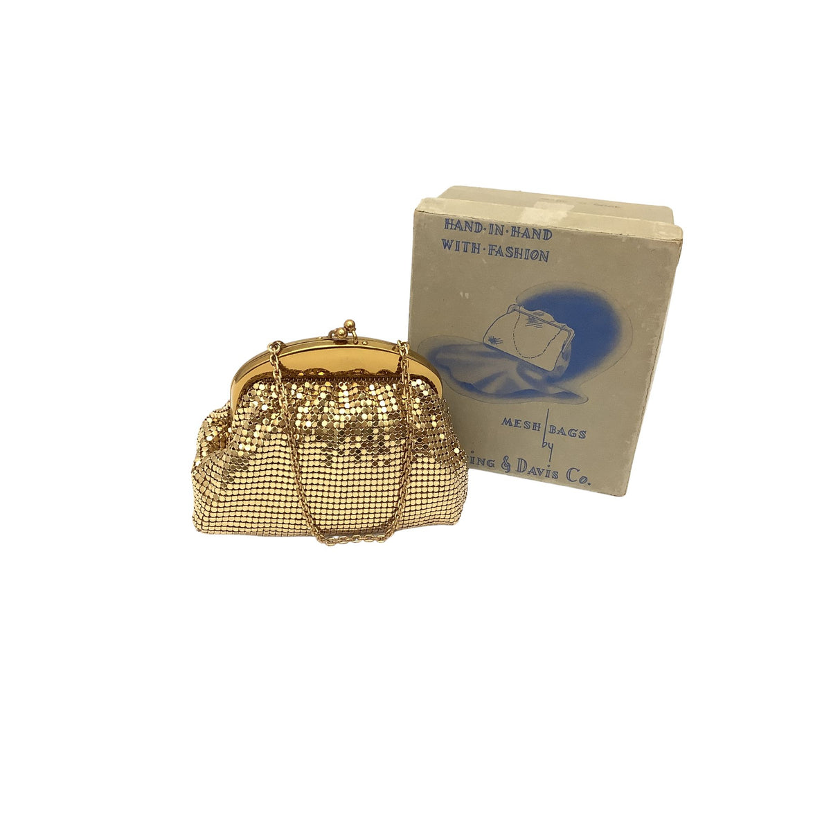 A Whiting & Davis gold-tone mesh clutch purse with a chain strap stands in front of its vintage paper box. The box is beige with blue text reading 'HAND-IN-HAND WITH FASHION' and 'ALEX & DAVIS Co.