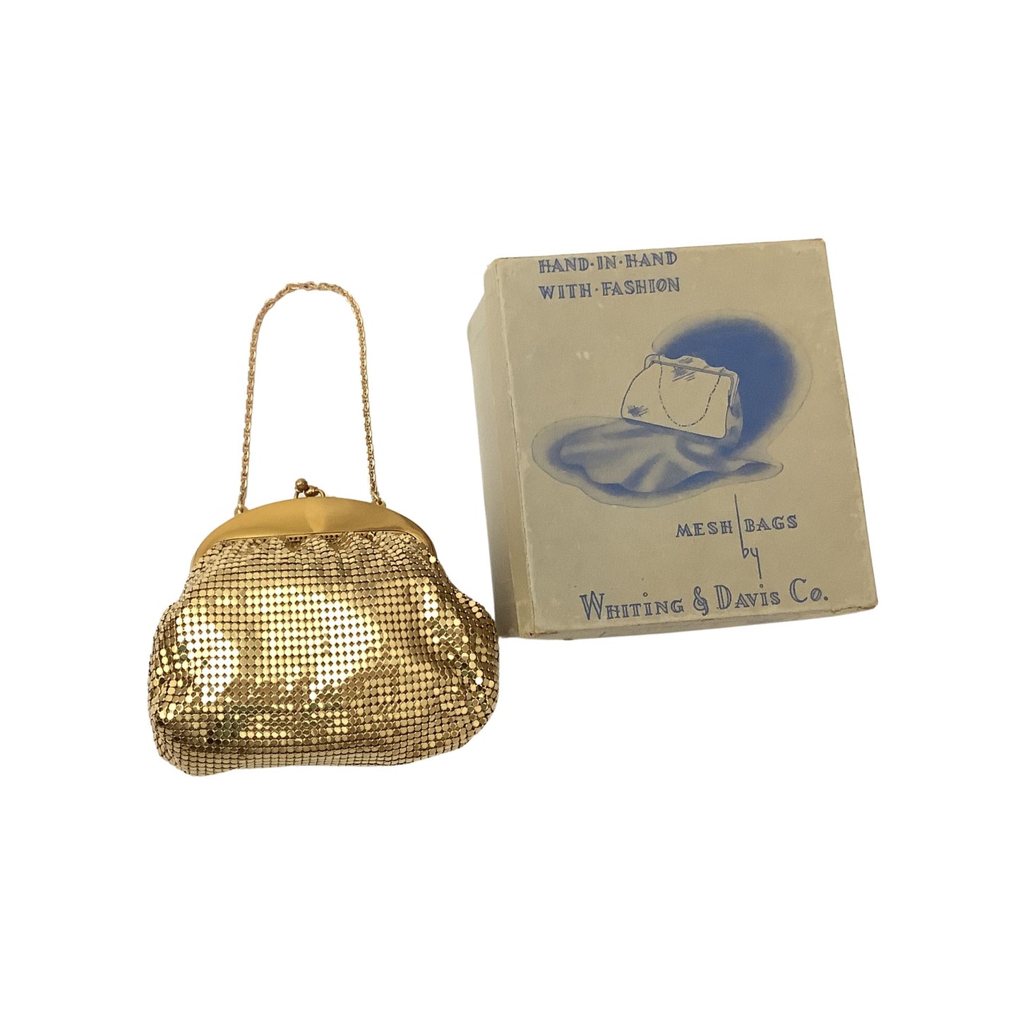 A vintage Whiting & Davis gold mesh handbag with a gold clasp and chain strap, displayed next to its original cream-colored packaging box printed with blue text and an illustration.