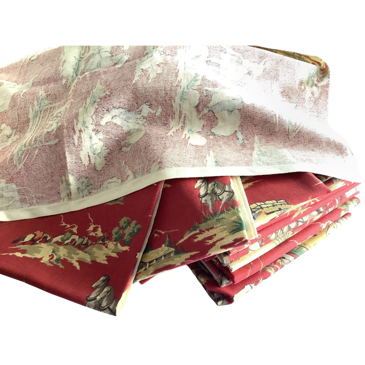 A stack of folded patterned fabrics or textiles on a white background, showing a backside of fabric on top and a red southwestern scenic print with horses and figures visible in folded fabric beneath.