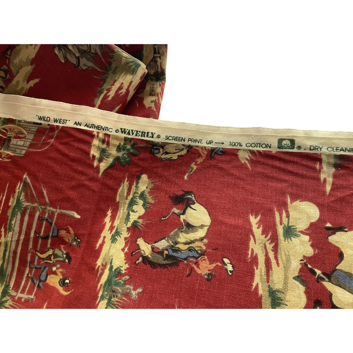 A folded piece of vintage Western-themed cotton fabric with a red background and a detailed print of cowboys, cattle, and desert landscapes. The fabric has a cream-colored selvage edge printed with text including 'WAVERLY'.