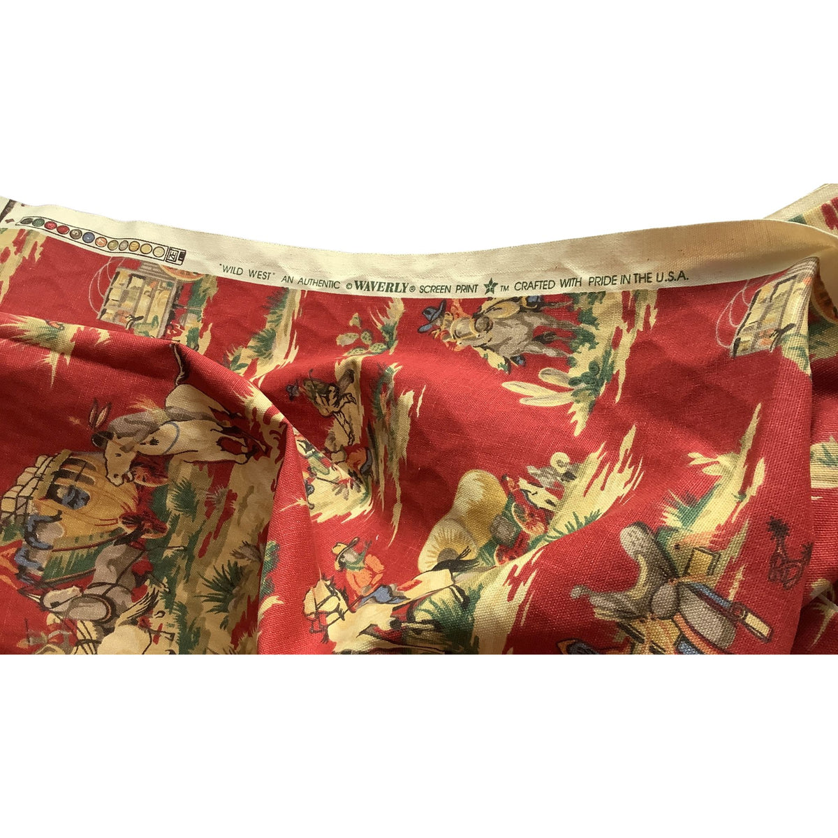 A close-up of a vintage patterned fabric, likely a quilt or textile, featuring a red background with a detailed cowboy and cattle scene in beige, green, and brown. The inner band shows the brand 'WILD WEST' and manufacturing details.