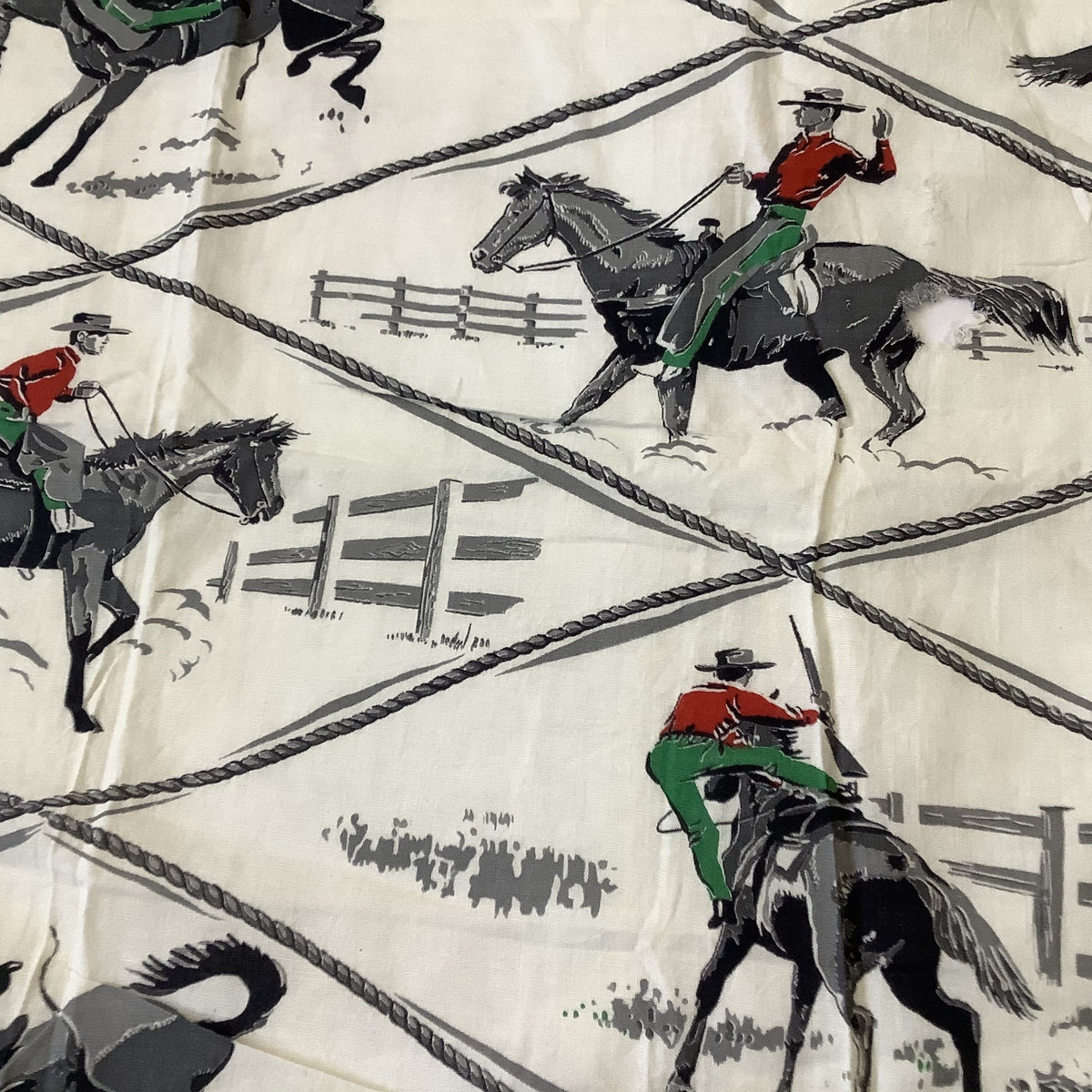 Vintage cowboy fabric in white cotton featuring a rustic western print of black horses, riders in red and green, and gray rope details.